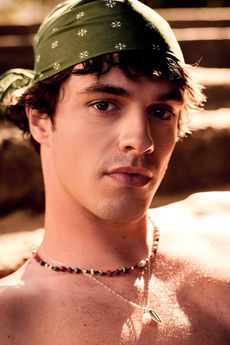 Close portrait of Francesco Ruggiero in a moss green dotted bandana tied across his forehead, layered beaded and pendant necklaces resting against his bare chest
