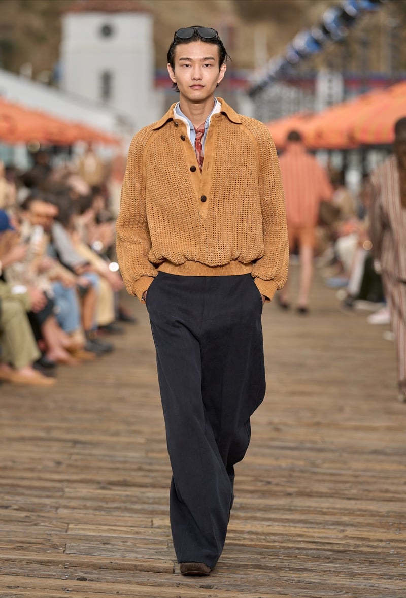 Male model wears a tobacco chunky knit half-zip polo with raglan sleeves over navy wide-leg trousers