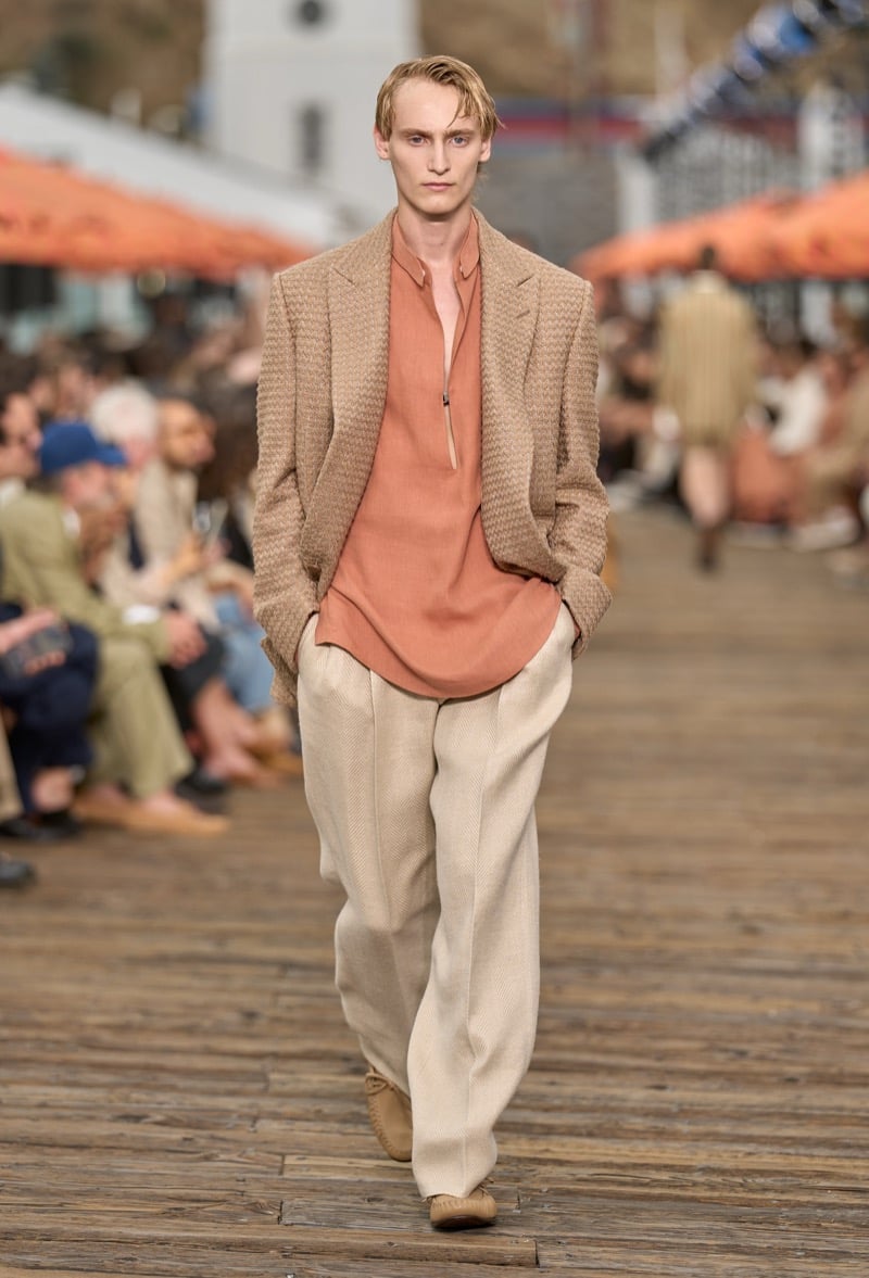 Male model wears a camel basketweave double-breasted blazer over a rust half-zip silk shirt with cream wide-leg trousers and tan moccasins