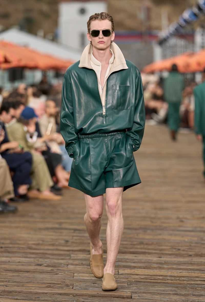 Male model wears a hunter green leather half-zip pullover with cream collar over matching leather shorts and tan suede moccasins