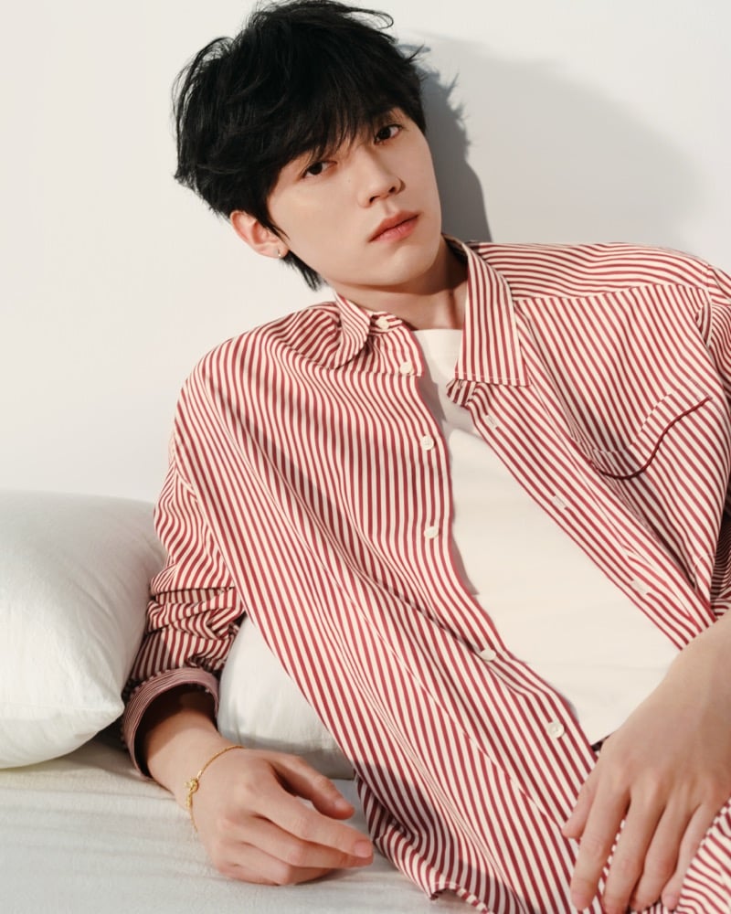 Zhou Yiran leans back against a pillow in a red and cream striped shirt layered over a white T-shirt, wearing a gold bracelet, for Ami Paris' Sweetheart capsule