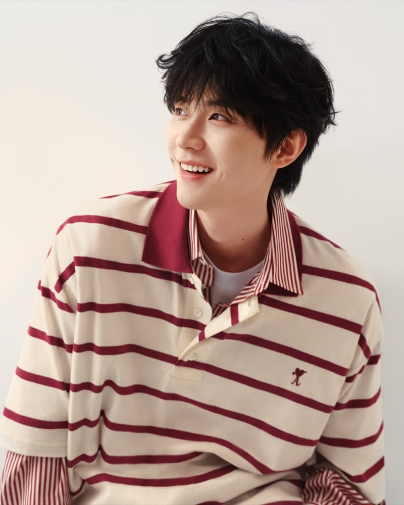 Zhou Yiran smiles in a cream and burgundy striped rugby polo with a contrast collar and embroidered Ami heart logo, for Ami Paris' Sweetheart capsule
