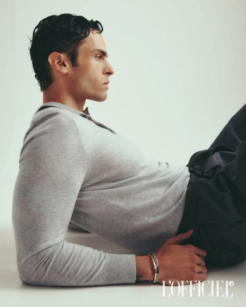 Baptiste Giabiconi reclines in profile wearing a gray sweater against a plain studio backdrop