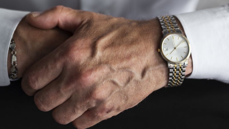 A close-up of two clasped hands, one wearing a two-tone bracelet watch with gold and steel links