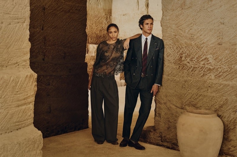 Francisco Henriques in a double-breasted suit with a model in an embellished top between carved stone pillars, a large ceramic urn beside them, for Brunello Cucinelli's fall 2026 edit