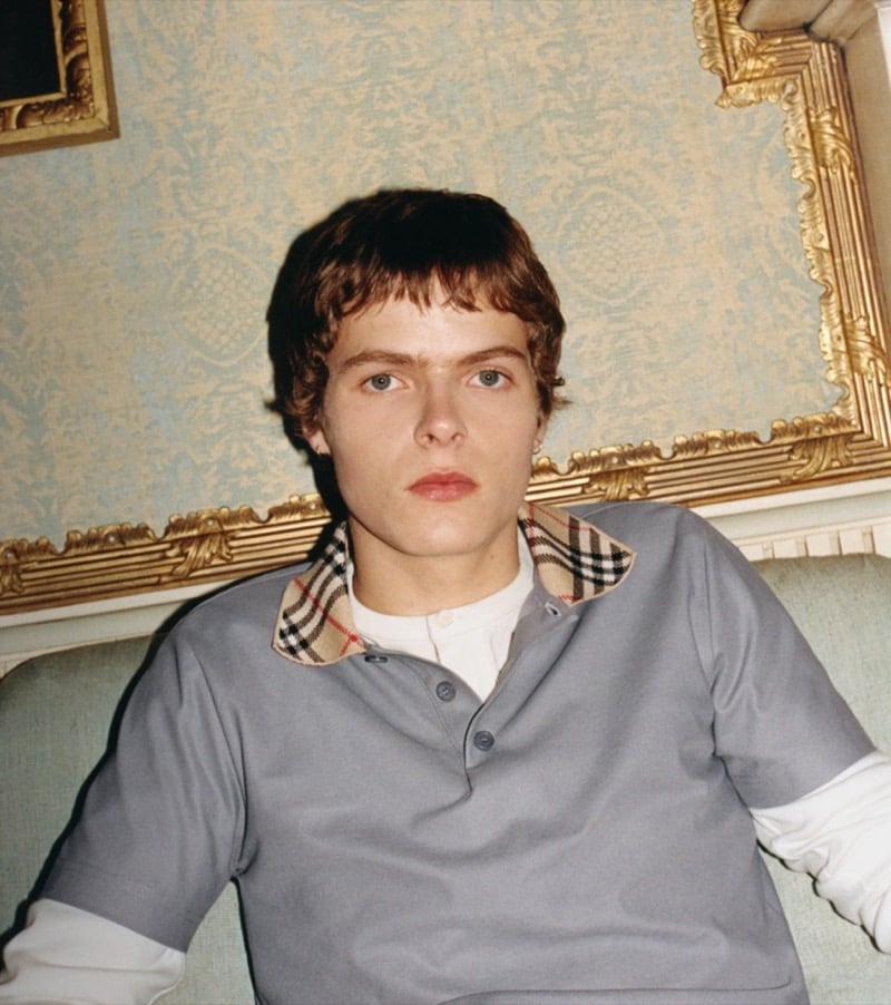 Close-up portrait of Moses Martin in a gray polo with a Burberry check collar in front of a gilded frame