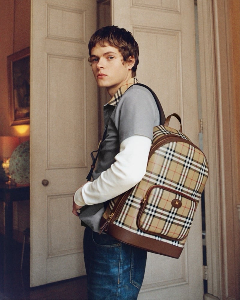 Moses Martin glances back in a doorway wearing a check collared polo and carrying Burberry's House Check backpack