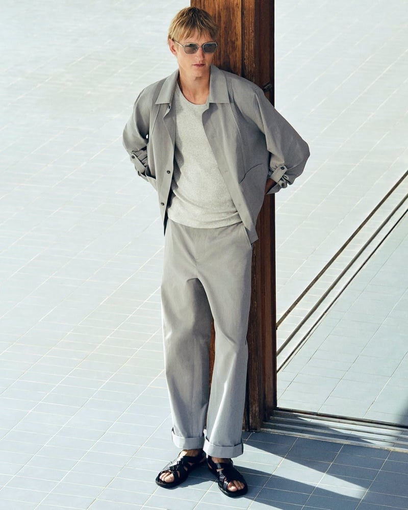 Pierrick Grégoire in a stone-colored unstructured jacket, gray T-shirt, and cuffed trousers with black sandals