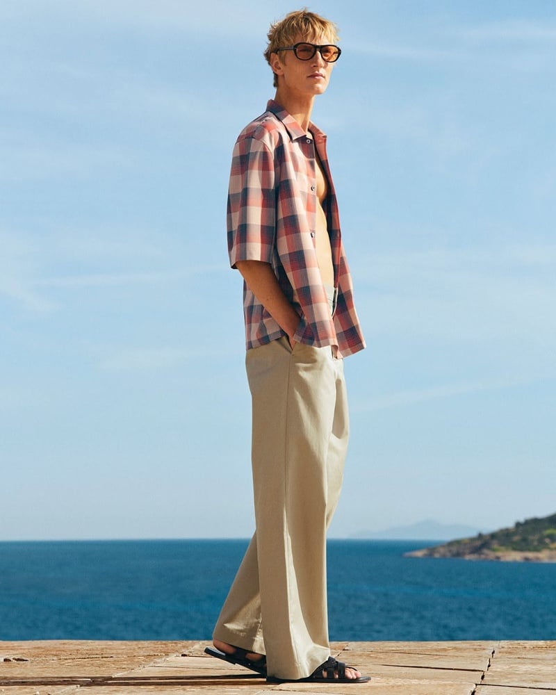 Pierrick Grégoire in an open red and blue check shirt and tan wide-leg trousers with sandals and sunglasses