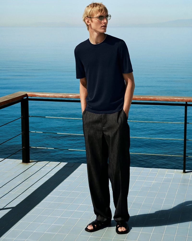 Pierrick Grégoire in a T-shirt and dark trousers standing by a railing overlooking the sea, hands in his pockets