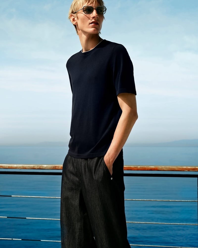 Close-up of Pierrick Grégoire in a T-shirt and dark trousers by the sea, one hand in his pocket