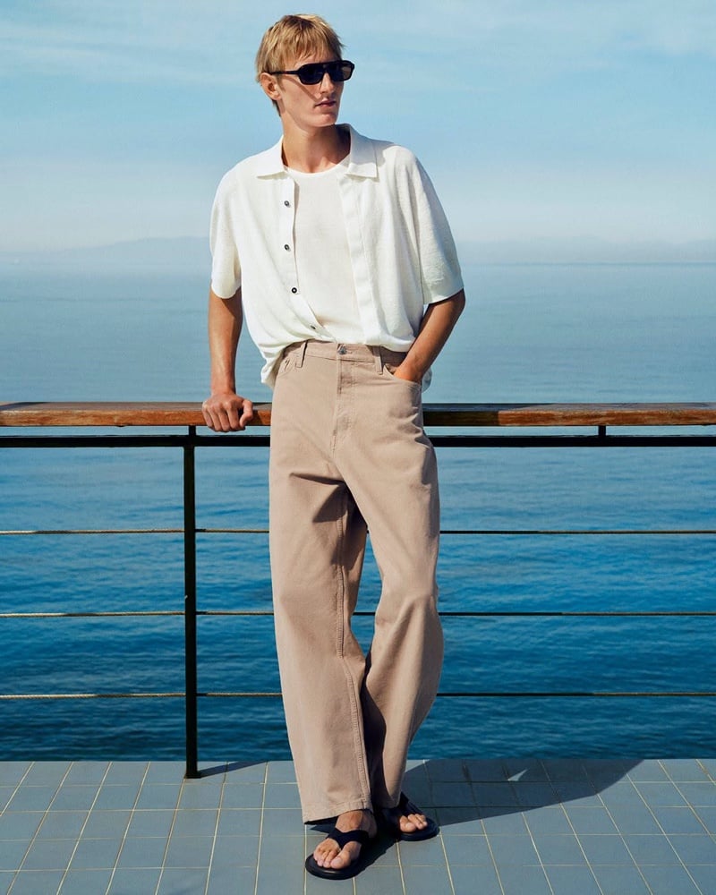 Pierrick Grégoire in a white waffle-knit camp shirt and tan trousers with black sandals by the sea