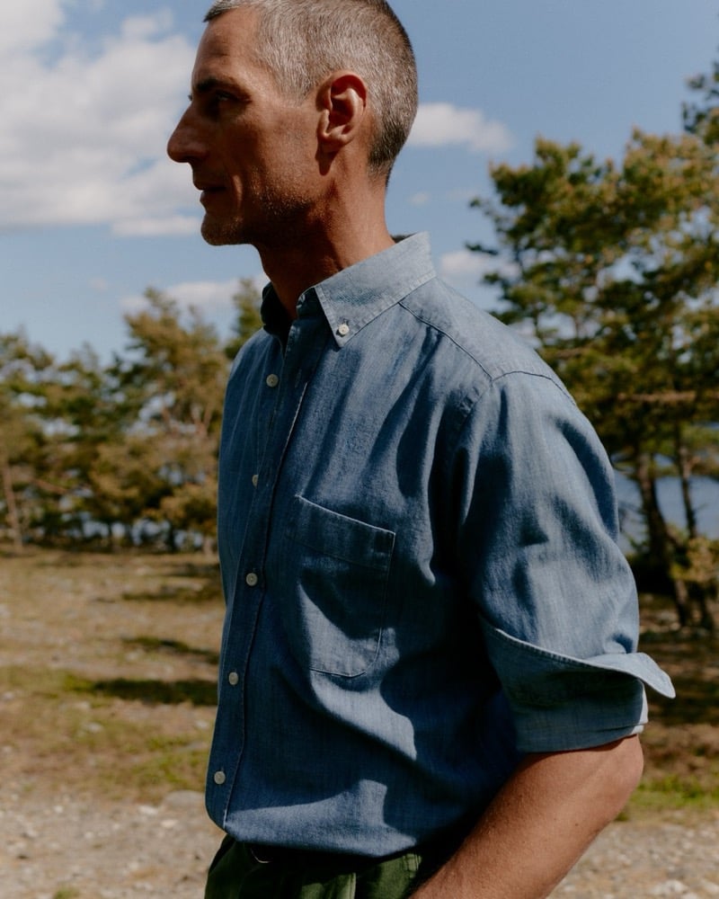 Axel Hermann in a chambray shirt with a chest pocket, pine trees and the sea in the background