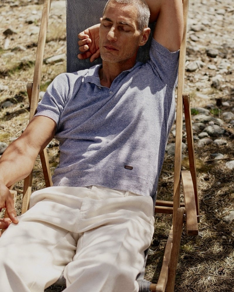 Axel Hermann reclines in a wooden deck chair wearing a heathered polo and cream trousers