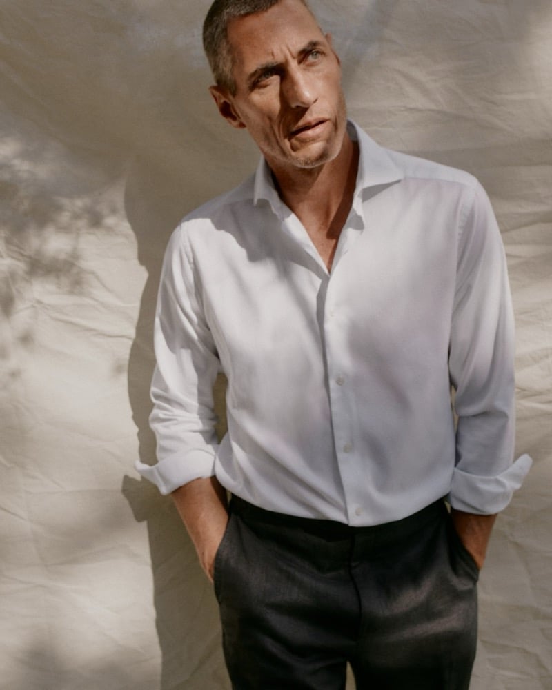Axel Hermann in a white shirt and dark trousers standing against a canvas backdrop