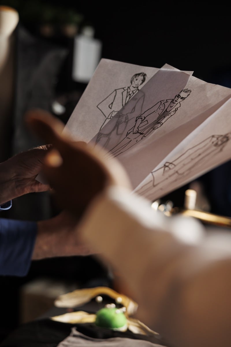 A hand flips through pages of original fashion sketches and illustrations