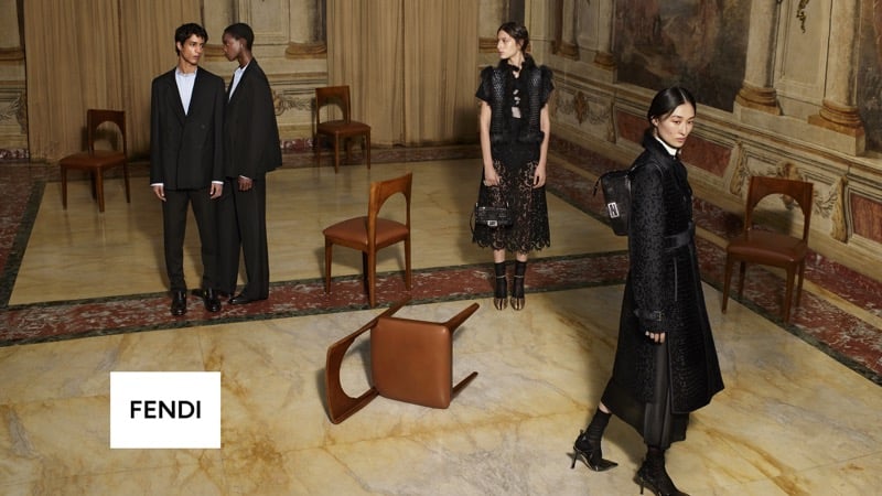 Mansur Lefqir and Faith Johnson stand together in matching dark tailored suits at the back of a frescoed room, while Chu Wong in a lace dress and Serena Sefyan in a long dark coat cross the marble floor past an overturned chair