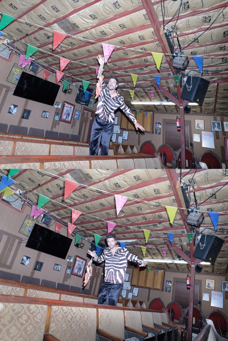François Arnaud reaches to catch a flying object under strings of colorful pennant flags in a zebra-print shirt