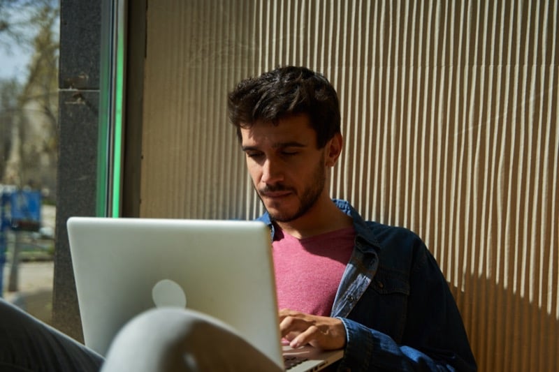 A designer types on a laptop at an outdoor café table while searching for freelance clients
