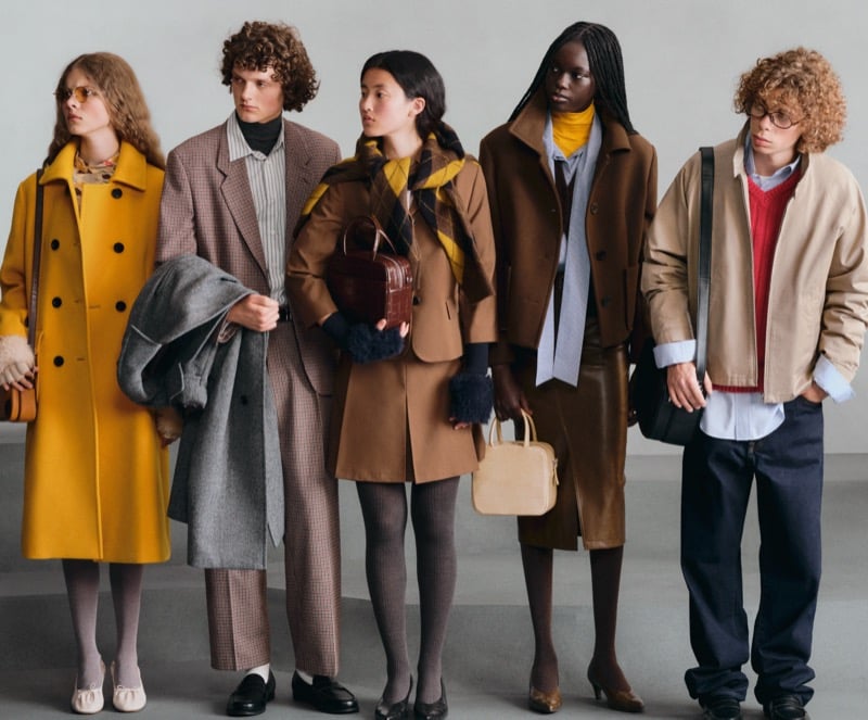 Five GU models in a line wearing a mustard coat, a checked coat, a camel trench with a plaid scarf, a brown blazer and skirt, and a tan jacket over a red sweater