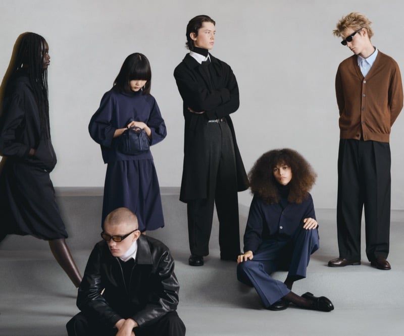 Six GU models grouped together in black leather, tailored coats, and knitwear in a moody neutral palette