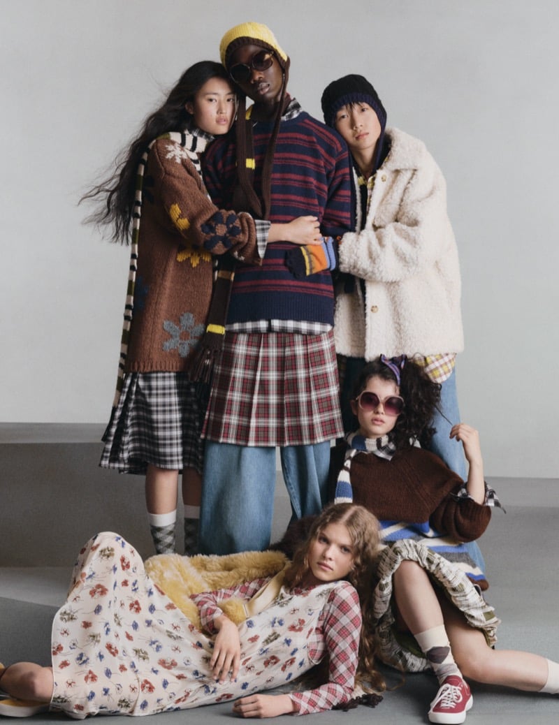 Five GU models grouped together in a patterned cardigan, a striped sweater with a plaid skirt, a shearling jacket, and a floral dress