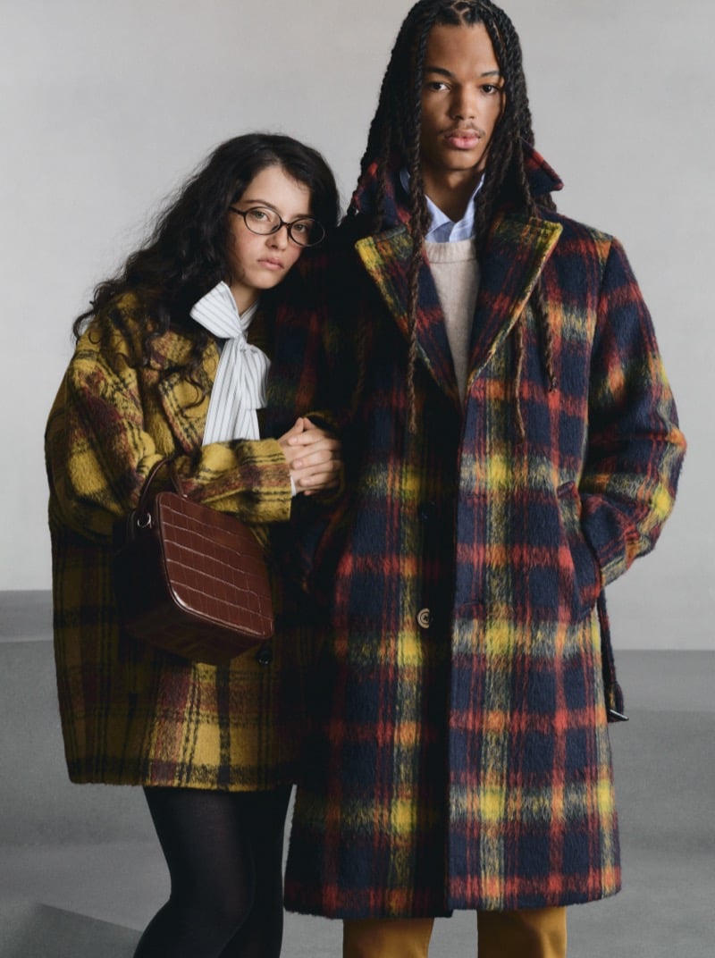 Two GU models in oversized plaid coats, one in a yellow-toned plaid, the other in a bold multicolor plaid, holding hands