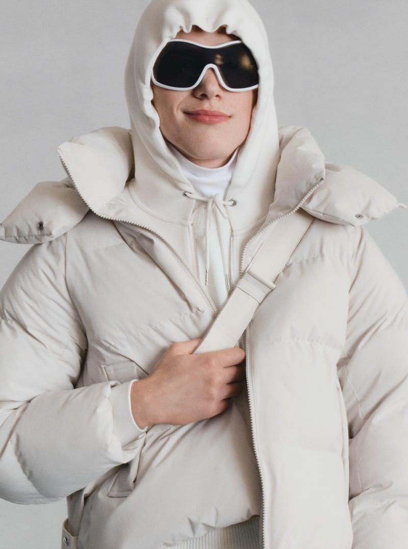 Close-up of a GU model in a light hooded puffer jacket and dark ski goggles, smiling