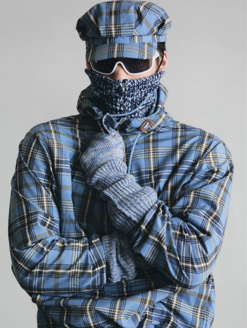 A GU model with his face fully wrapped in a knit turtleneck, wearing ski goggles, a plaid cap, and an oversized plaid jacket