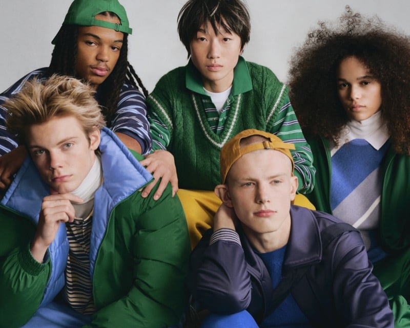 Five GU models grouped together in green sweaters, striped knits, and a puffer jacket in shades of blue, green, and yellow