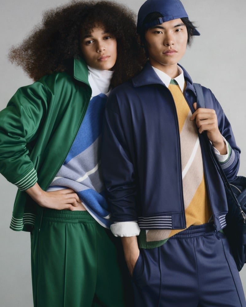 Two GU models in track jackets, one green with a colorblock sweater, the other deep blue with a backward cap and tan colorblock sweater