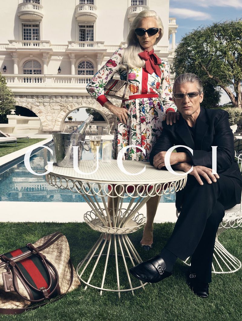 Elisabetta Dessy in a floral Gucci dress with a red bow stands behind Felix Friedman in a black suit at a table on a Monte Carlo hotel terrace