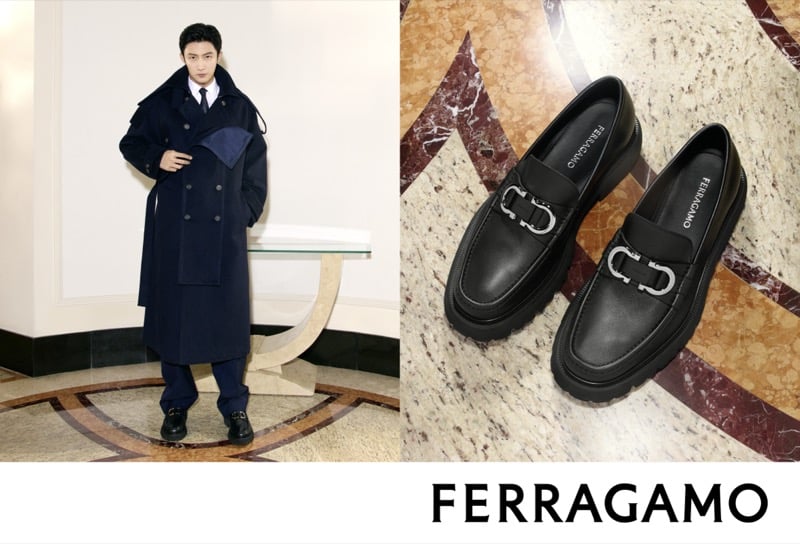 Huang Jingyu wears an oversized navy double-breasted trench coat, with a black leather Gancini-buckle loafer shown alongside