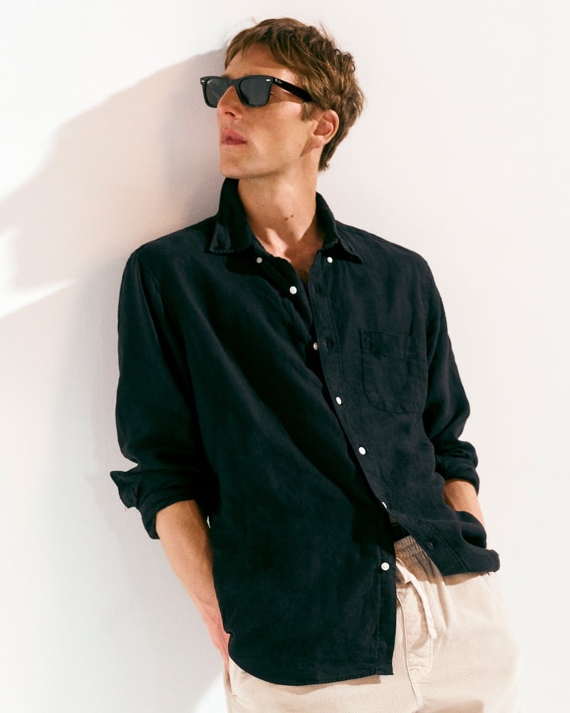 Quentin Demeester in a dark garment-dyed linen shirt and cream trousers leaning against a wall