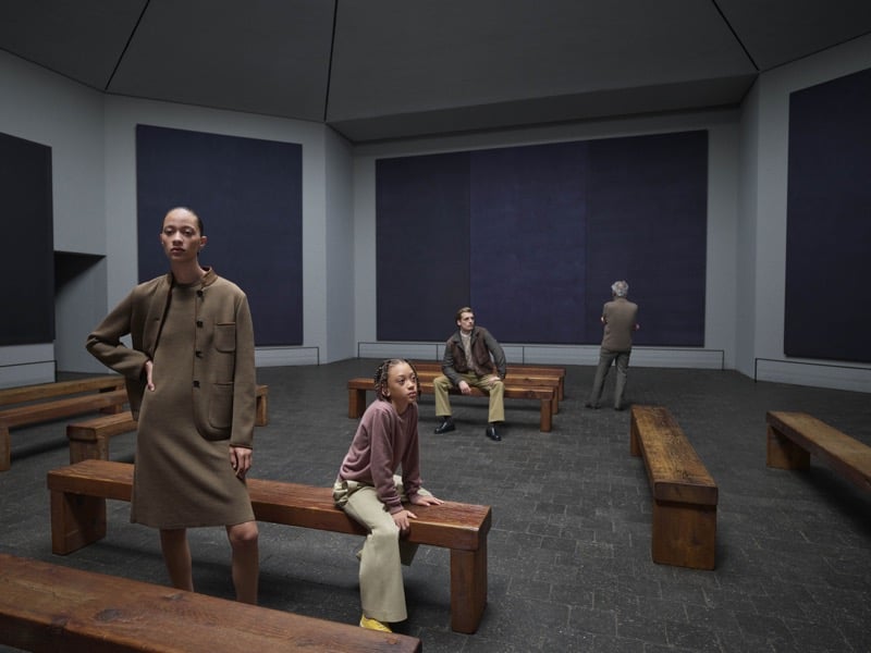 Four models sit and stand inside the Rothko Chapel, dressed in camel coats, knitwear, and trousers among dark canvases and wooden benches