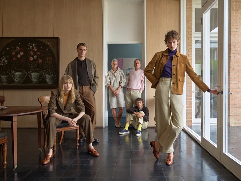 Members of the Loro Piana fall 2026 cast gather in a wood-paneled interior, dressed in suede jackets, knitwear, and wide-leg trousers