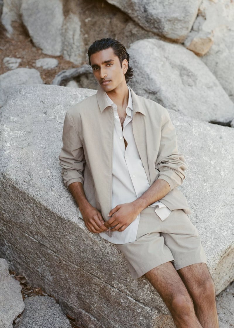Jeenu Mahadevan in a stone-colored shirt jacket seated on a large boulder