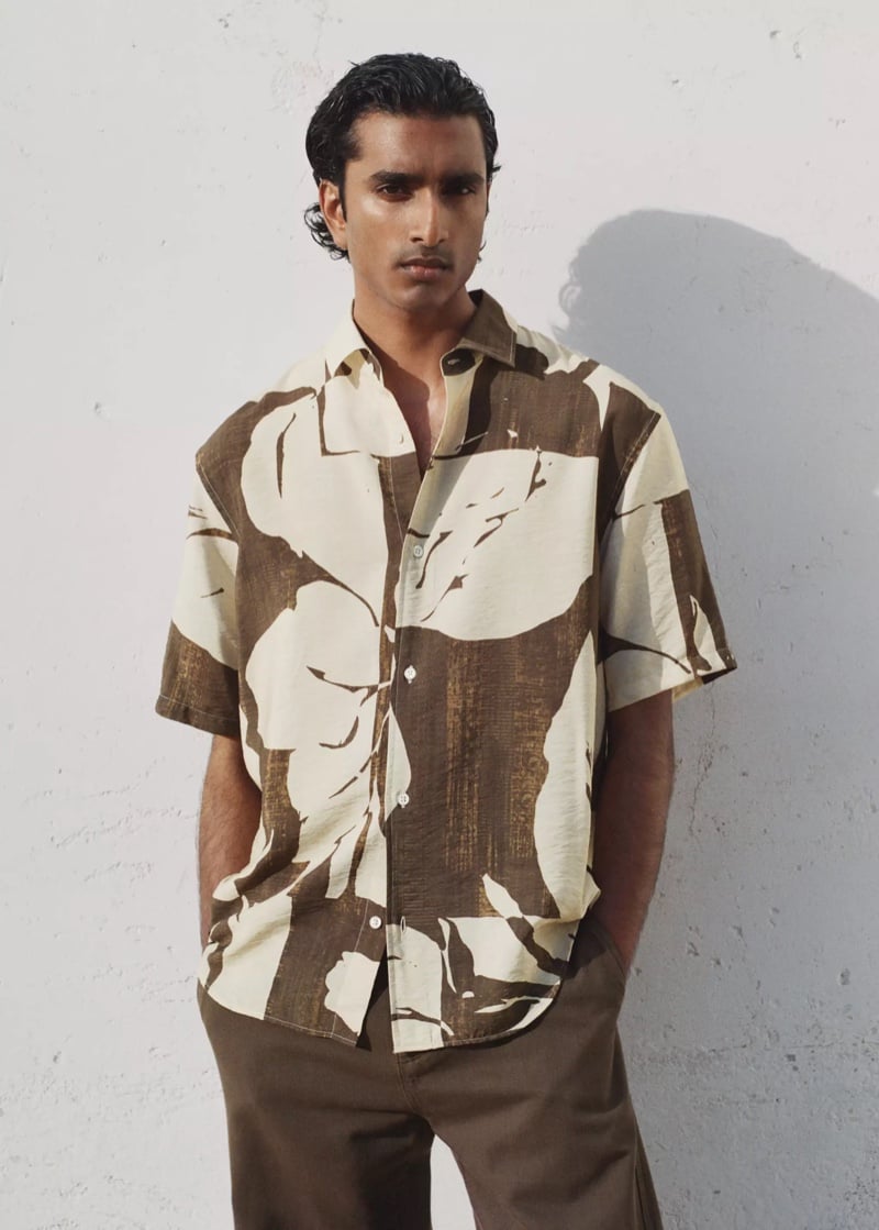Jeenu Mahadevan in a brown and cream abstract-print shirt and brown trousers with hands in his pockets