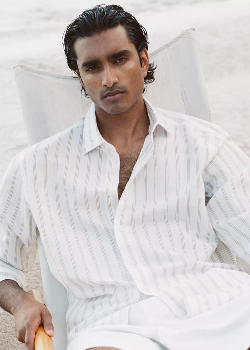 Jeenu Mahadevan in an open pinstripe shirt seated in a white beach chair