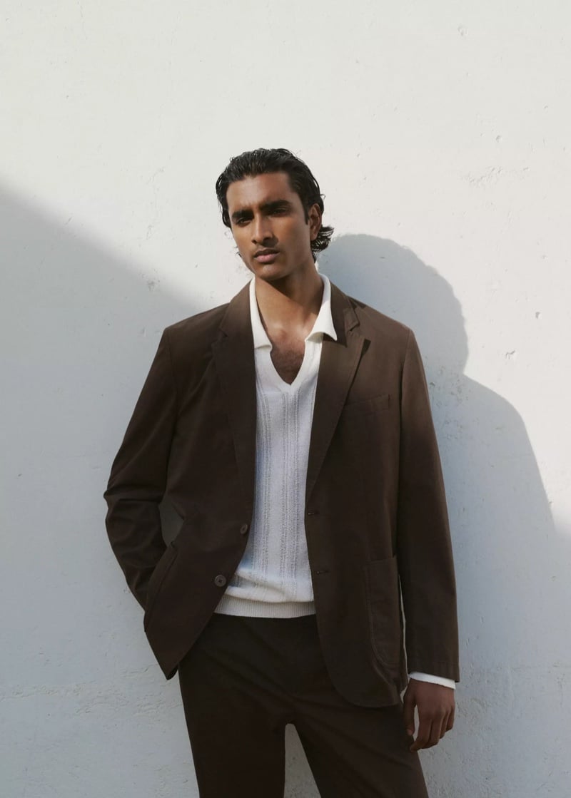 Jeenu Mahadevan in a brown blazer over a white knit polo against a white wall