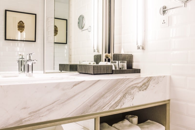Close view of a white marble bathroom vanity countertop with brass trim, a mirror, and folded towels beneath