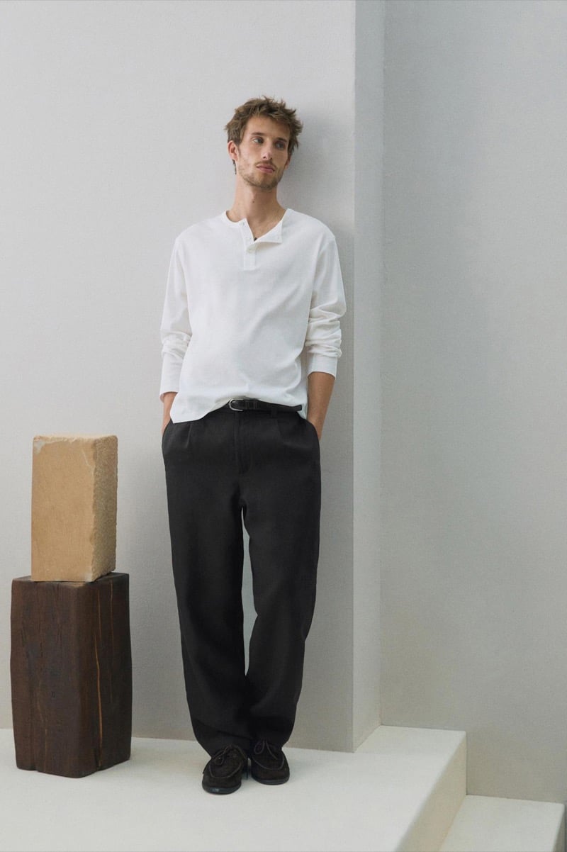 Aristide Deslandes wears a white henley and black trousers with black lace-up shoes