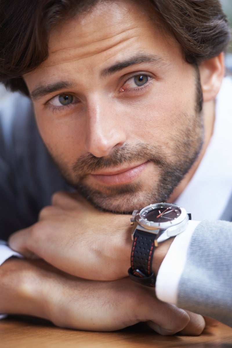 A bearded man rests his chin on his hand, wearing a sport watch with a black rubber strap