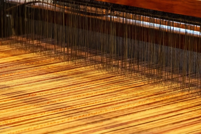 Rows of colored thread strung through a traditional loom inside a textile mill