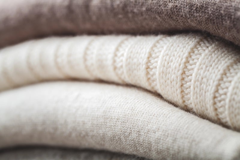 A stack of folded wool sweaters in cream and brown tones showing dense knit texture