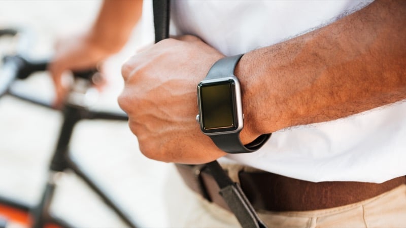 A man holding a bicycle wears a watch with a black rubber strap on his wrist