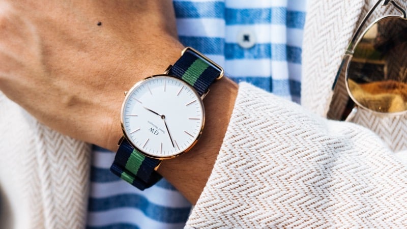A watch with a navy and green striped fabric strap worn with a striped shirt and cardigan