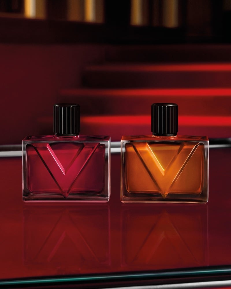 Two Valentino Vendetta Uomo bottles with a raised V motif sit on a glossy surface with red light streaks in the background