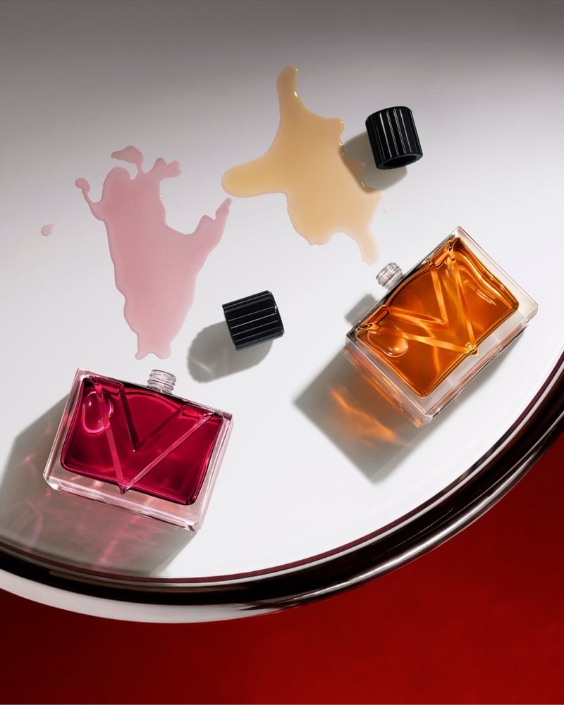 Valentino Vendetta bottles lie on their sides with pink and amber fragrance pooled around them on a white surface