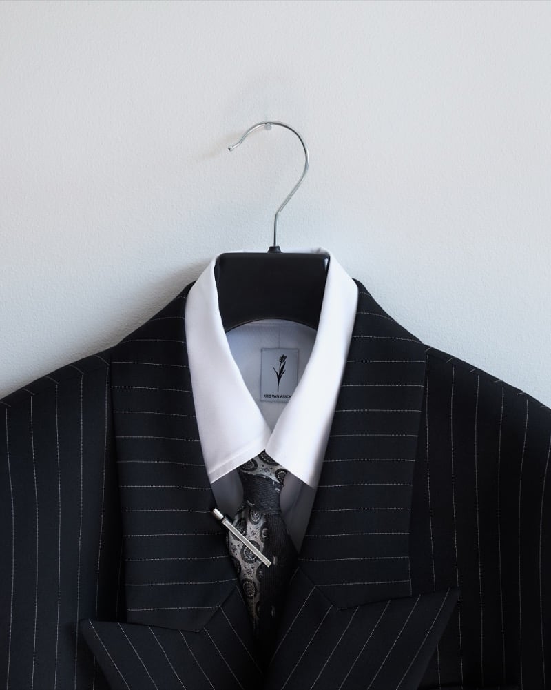 A striped KRISVANASSCHE suit on a hanger with a wide white contrast collar, a paisley tie, and a silver tie clip